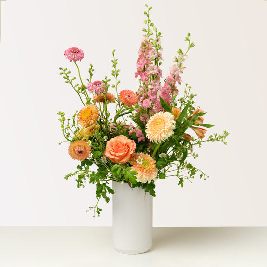 Tall pink and orange flower arrangement in white vase