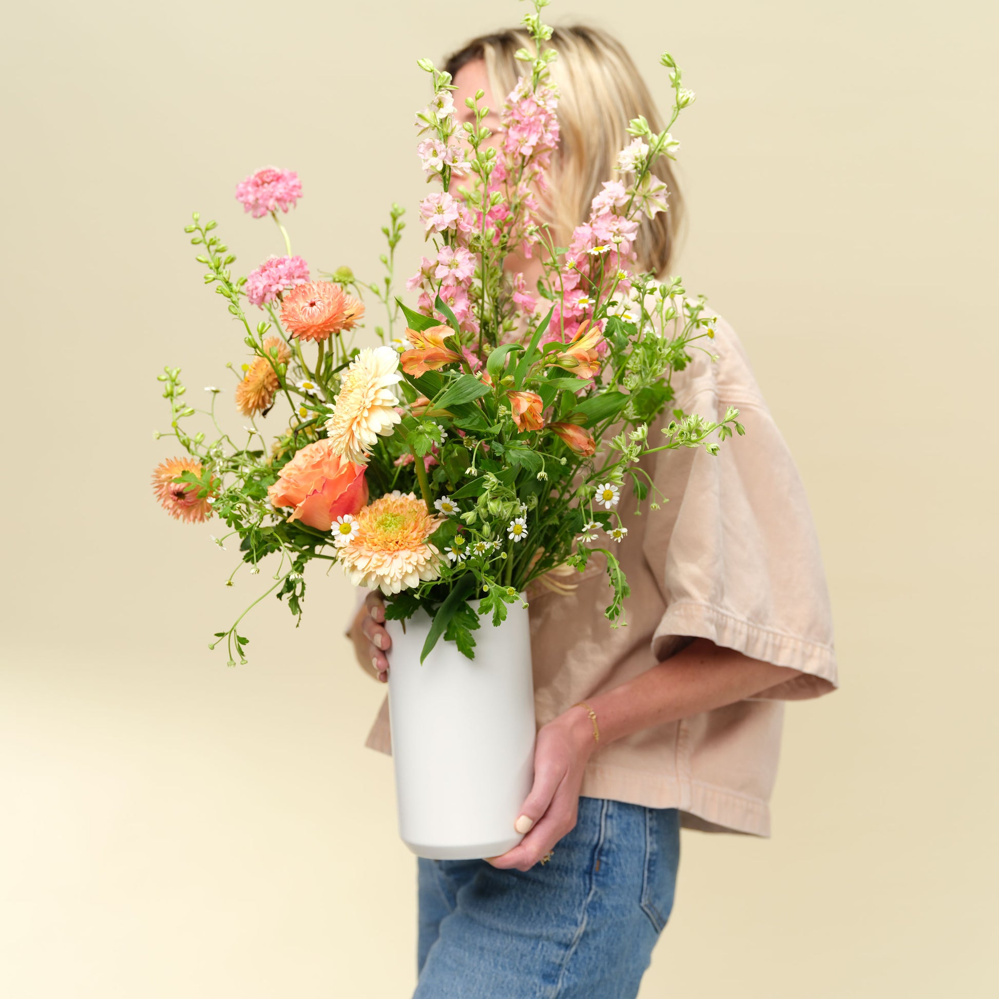 Woman holds tall pink and orange flower arrangement in white vase