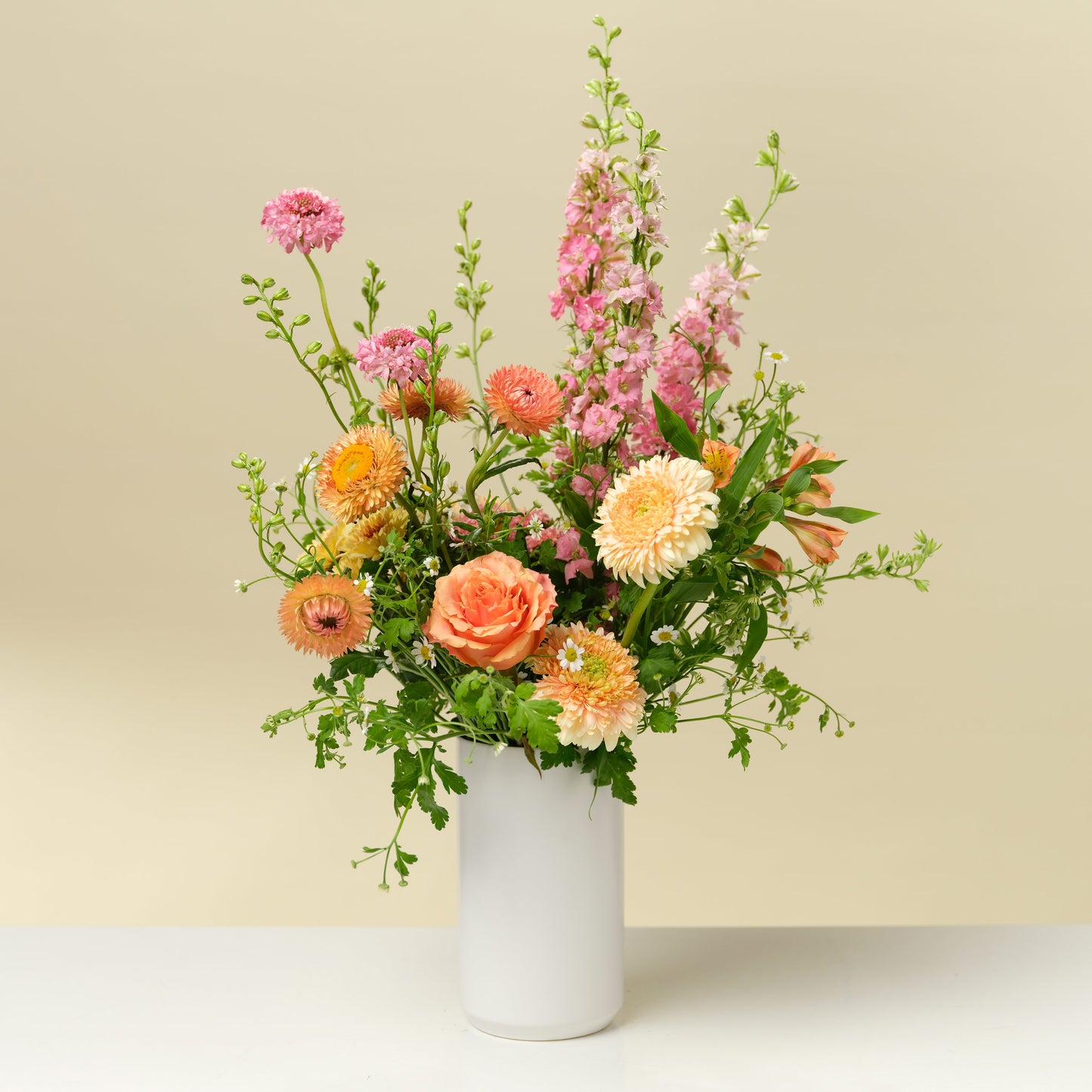 Tall pink and orange flower arrangement in white vase