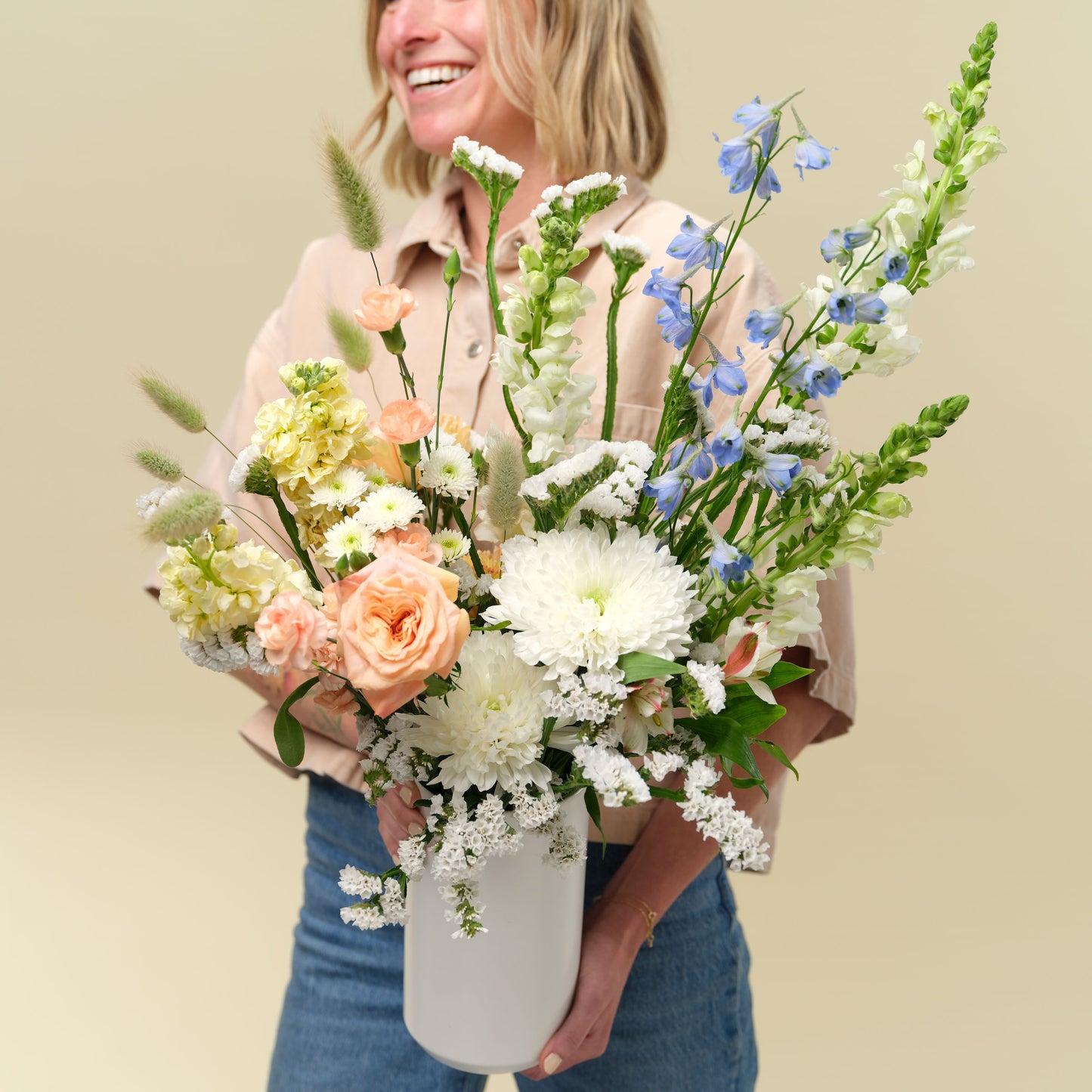 Woman holds white and pastel flower arrangement in white vase