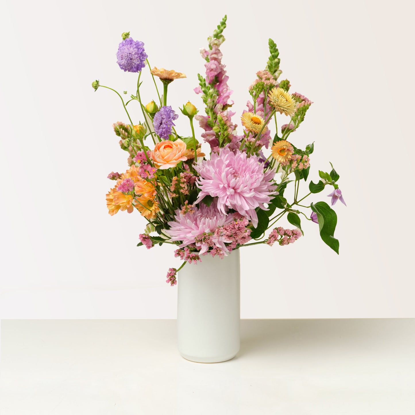 Tall blue, purple, pink, orange, and green flower arrangement in tall white vase