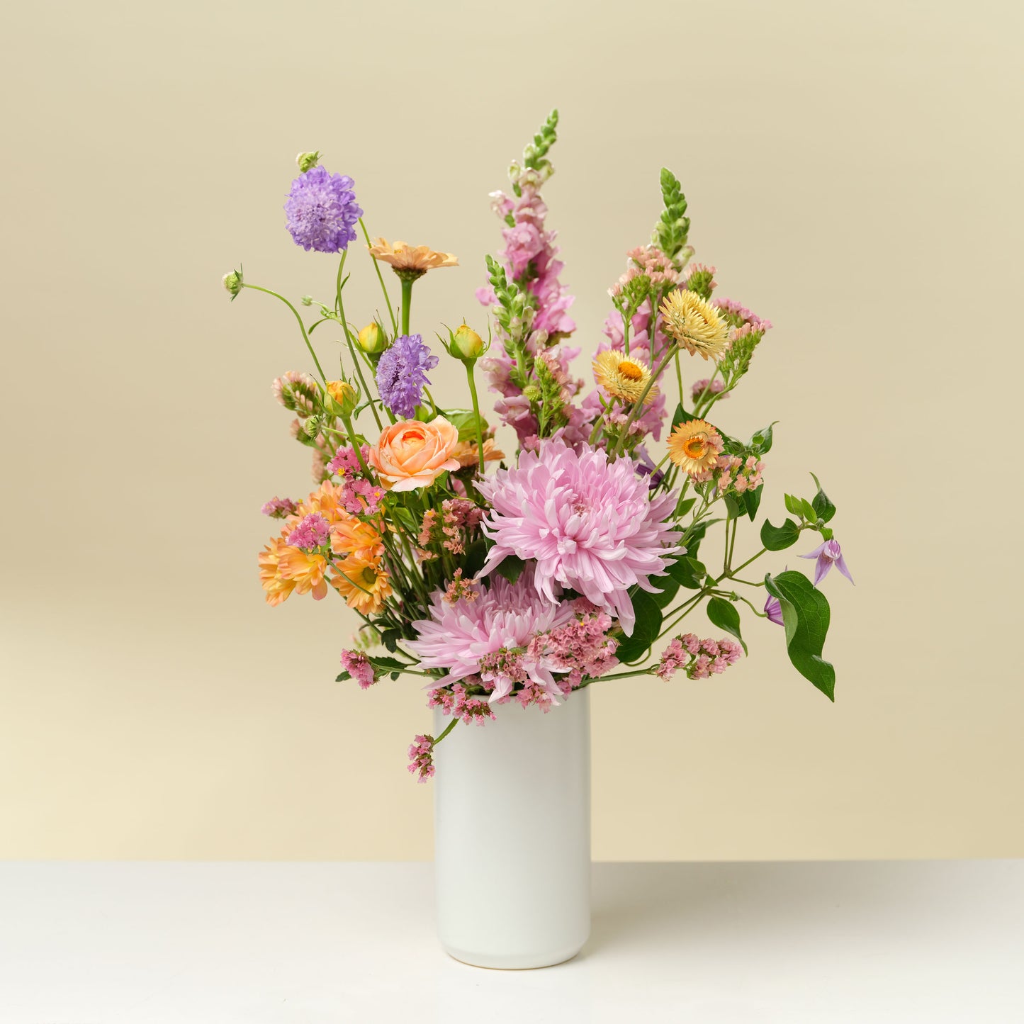 Tall blue, purple, pink, orange, and green flower arrangement in tall white vase