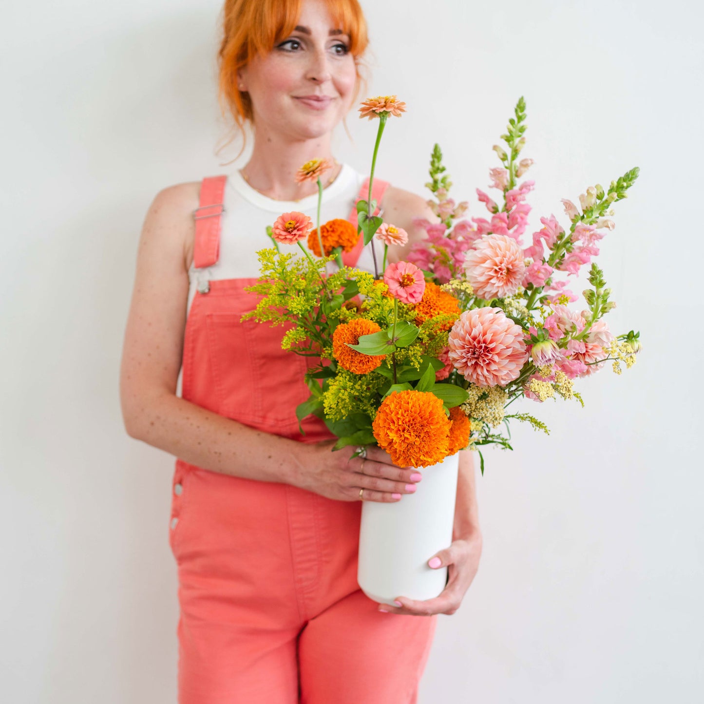 Woman holding tall pink and orange flower arrangement in white vase