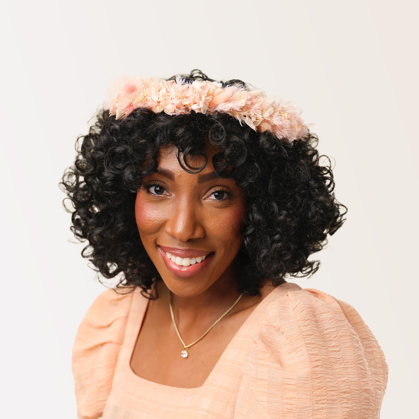 Woman with dark curly hair wearing pink dried flower crown