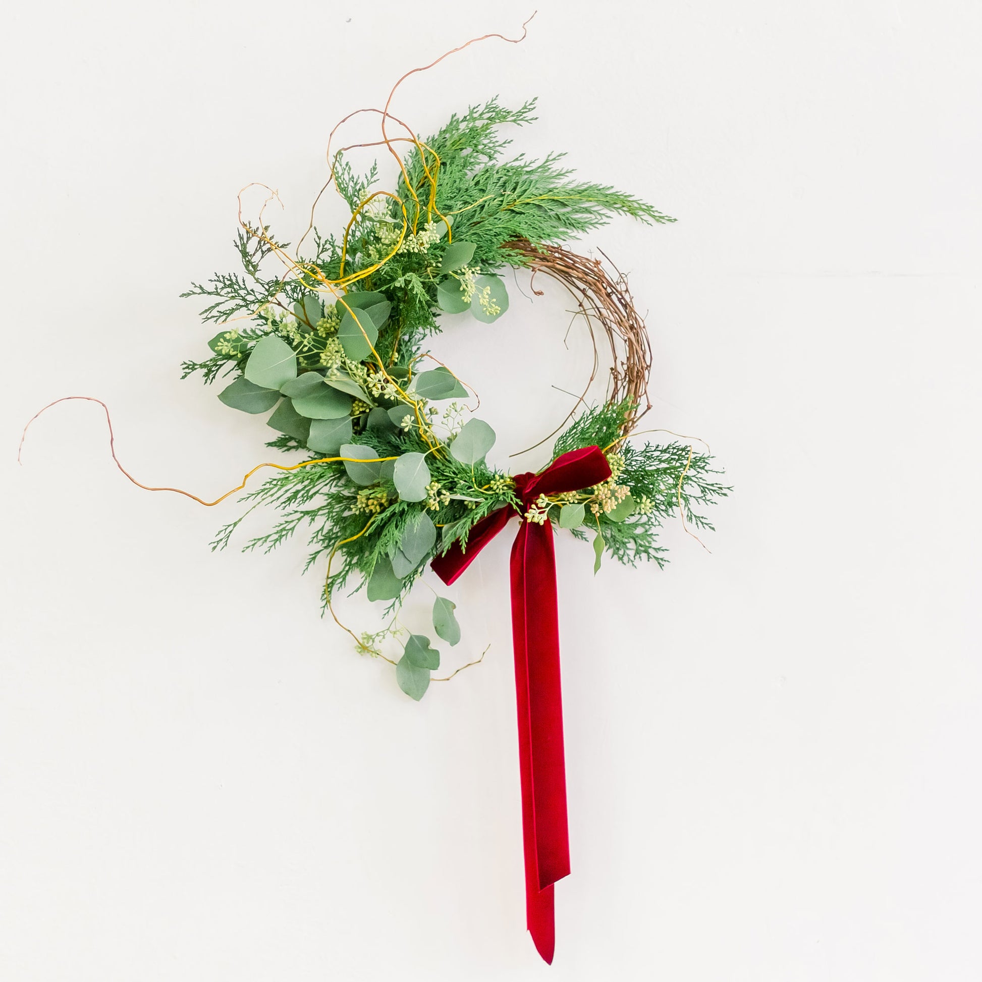 Winter Forest Wreath made with cedar and eucalyptus, tied with red ribbon