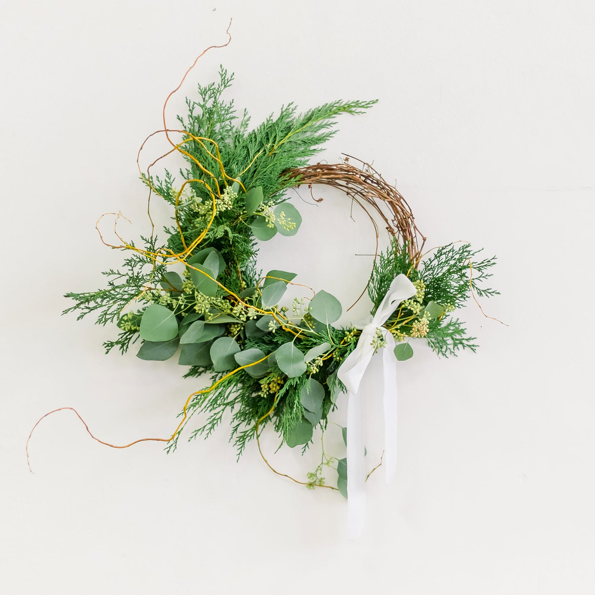 Winter Forest Wreath made with cedar and eucalyptus, tied with white ribbon