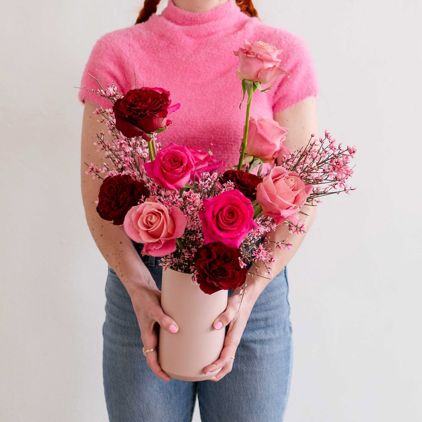 Young woman holding wild heart garden roses in a blush pink vase