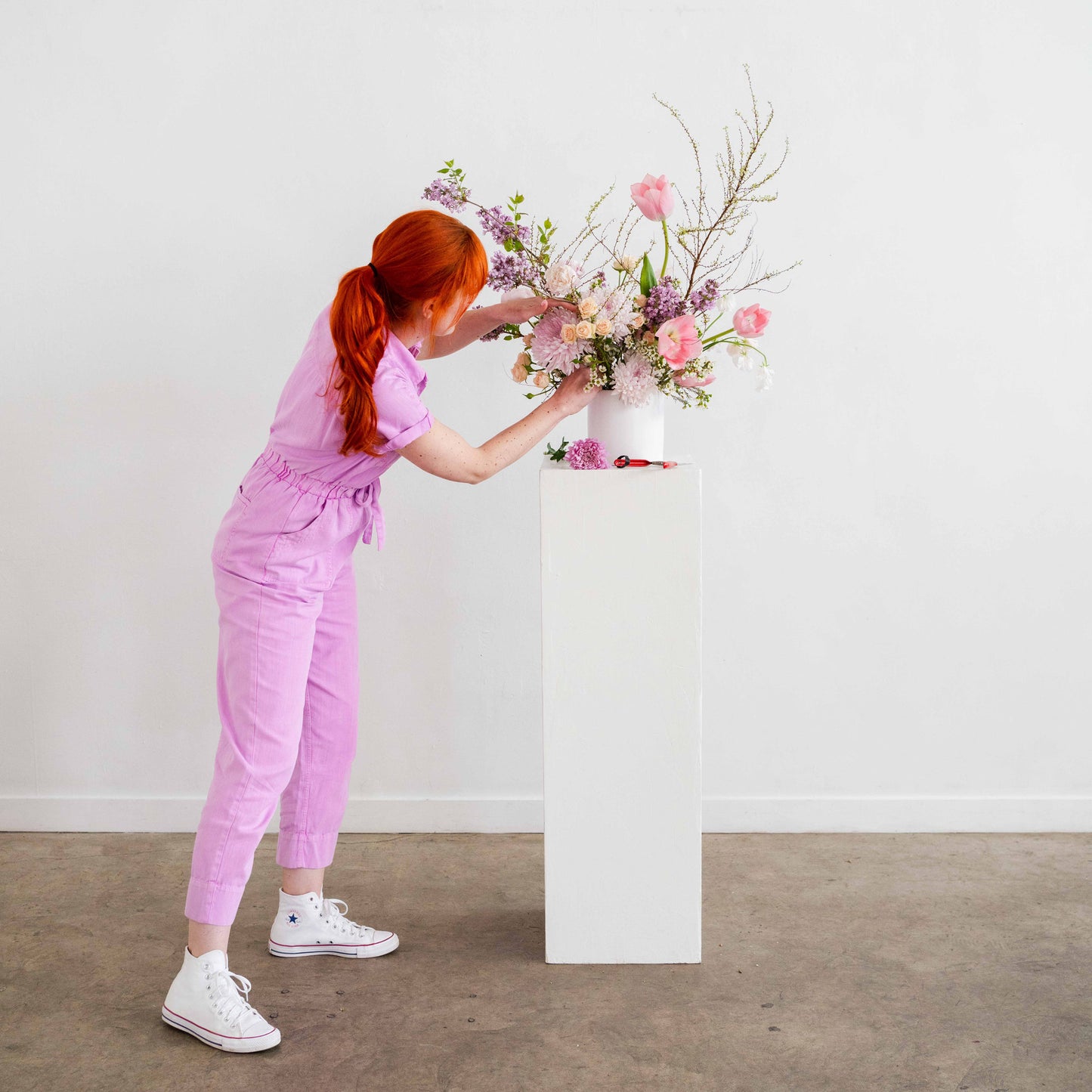 florist adjusts flowers on white wedding pedestal